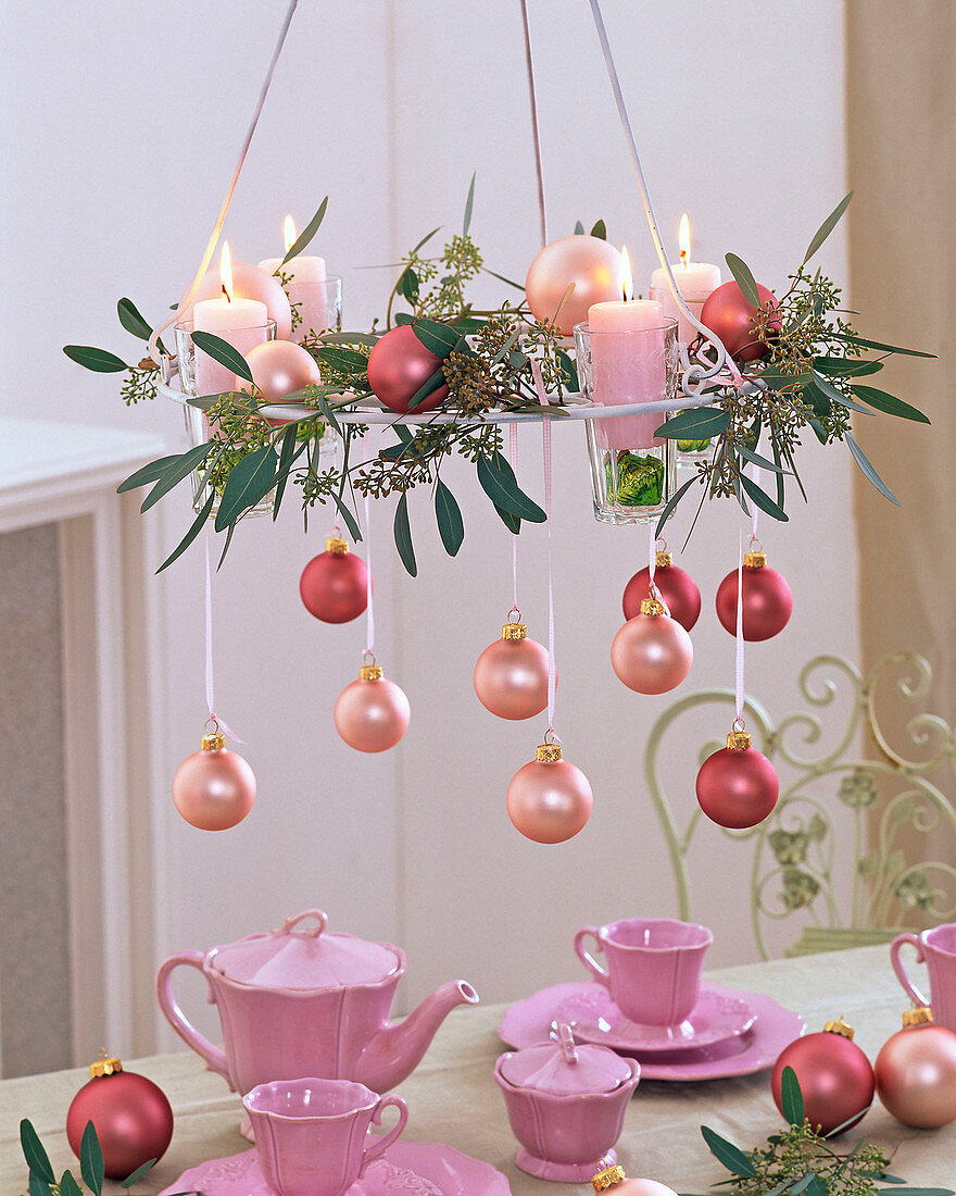 Ceiling hanging with eucalyptus, tree ornaments and four candles over pink tableware