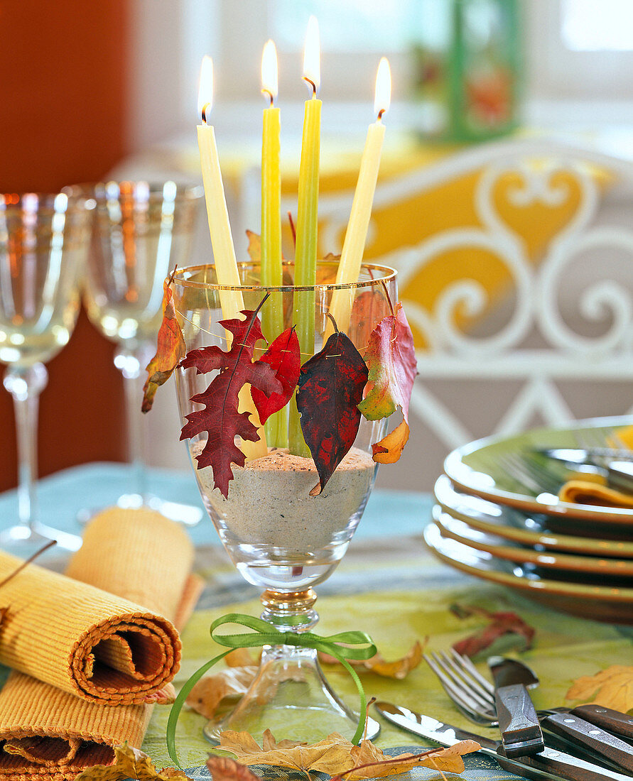 Autumn leaves on gold wire around glass with candles