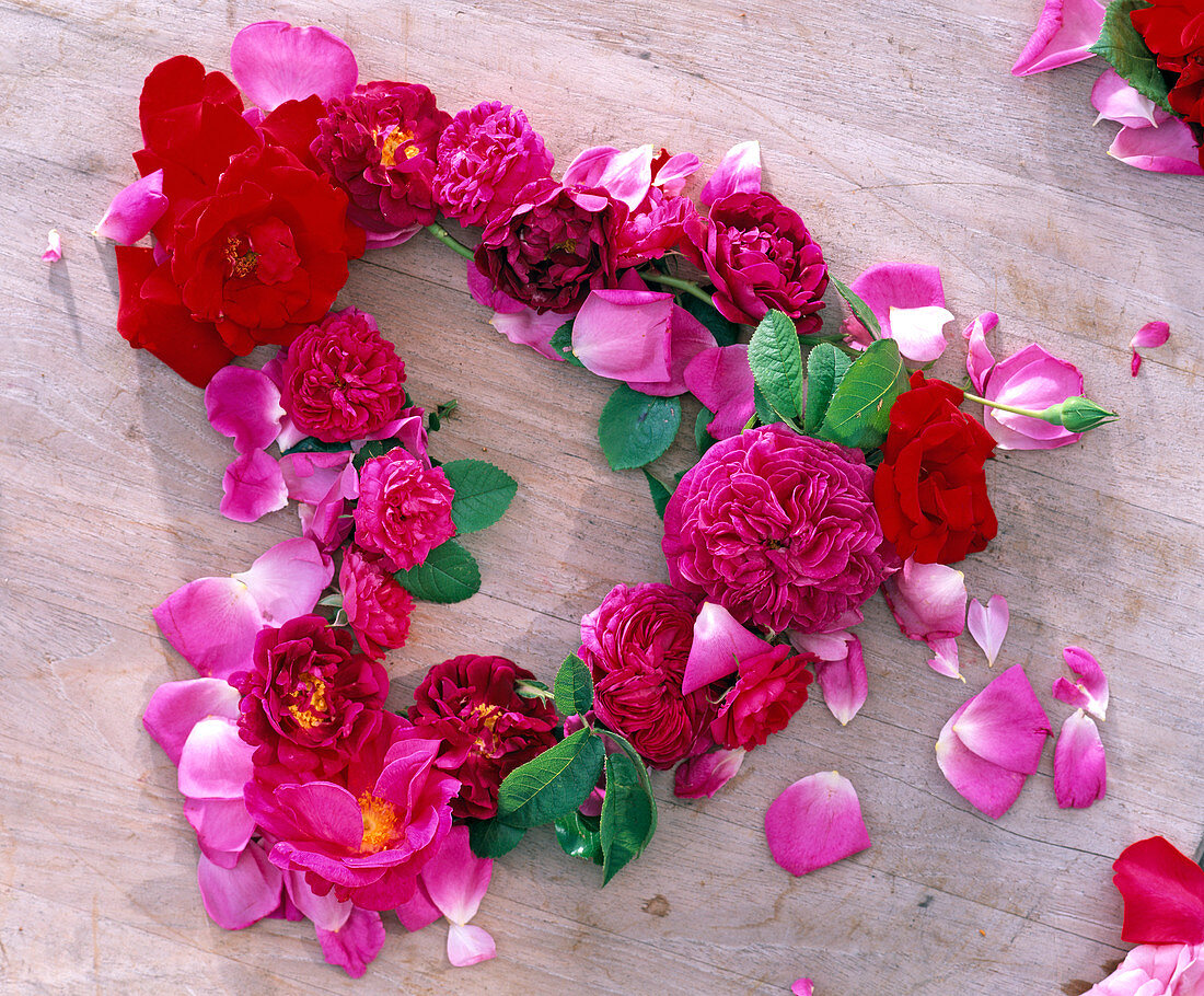 Heart of pink flowers (roses in pink and red) placed on wood, petals