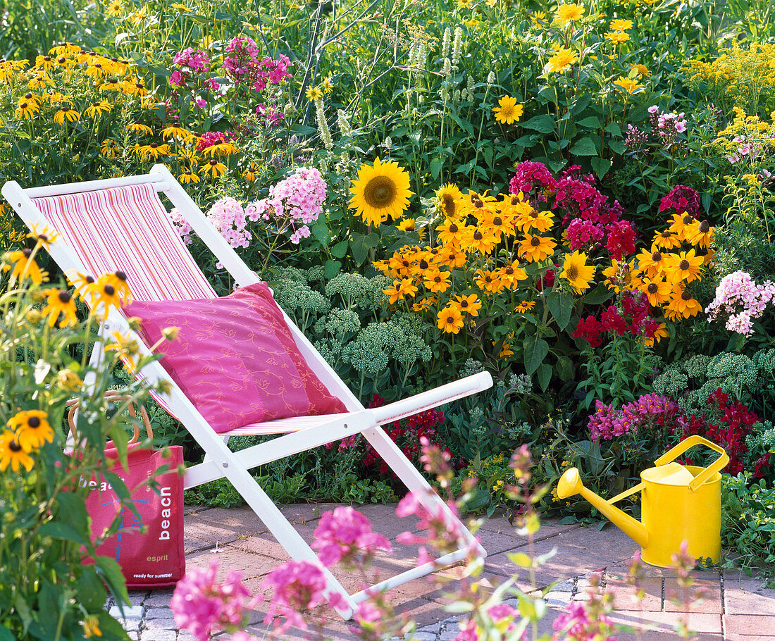 Folding deck chair on the flowering bed with Rudbeckia fulgida and hirta