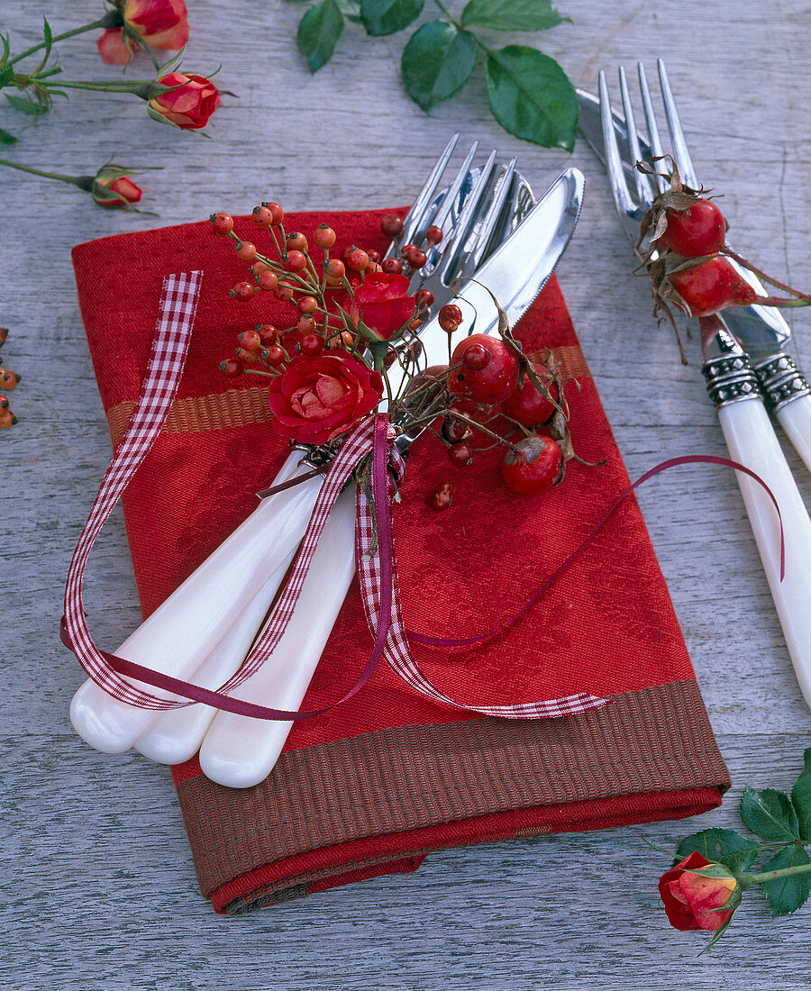 Small bouquet of pink (red roses and rose hips) on cutlery on napkin