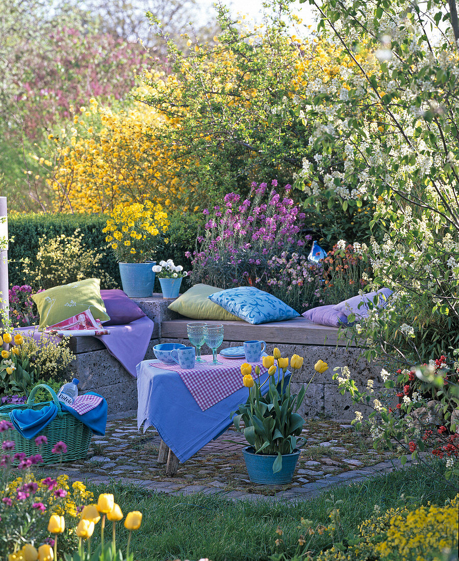 Gemauerte Bank an kleiner Terrasse, umrahmt von Frühlingsblumen