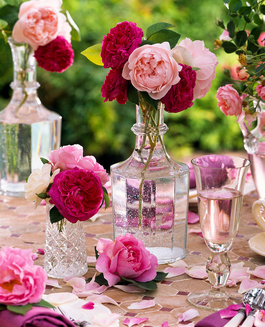 Pink (roses) in glass bottles on mosaic table with petals, glass