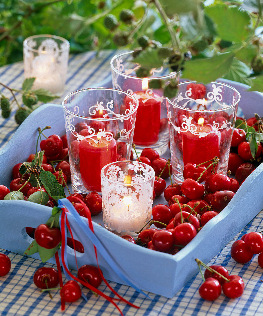 Glasses with pillar candles on a tray with Prunus (cherries)