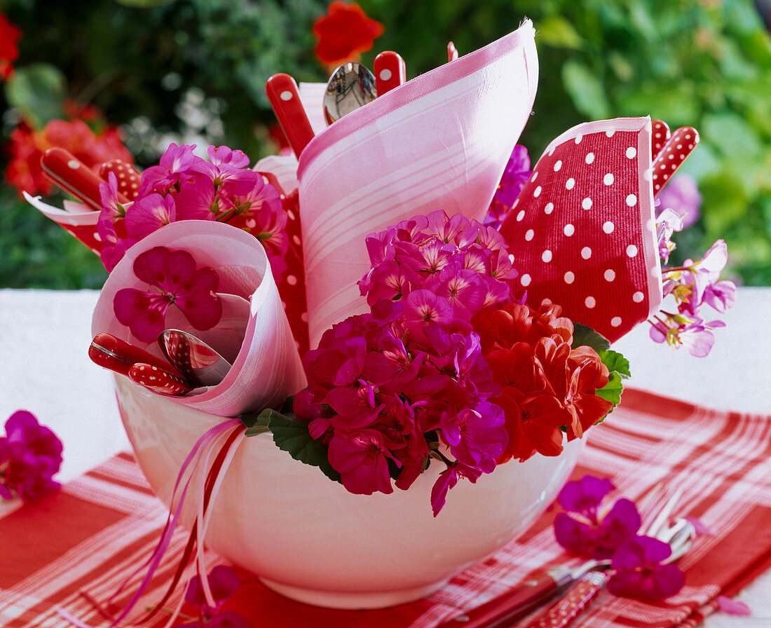 Pelargonium in bowl with rolled napkins with cutlery