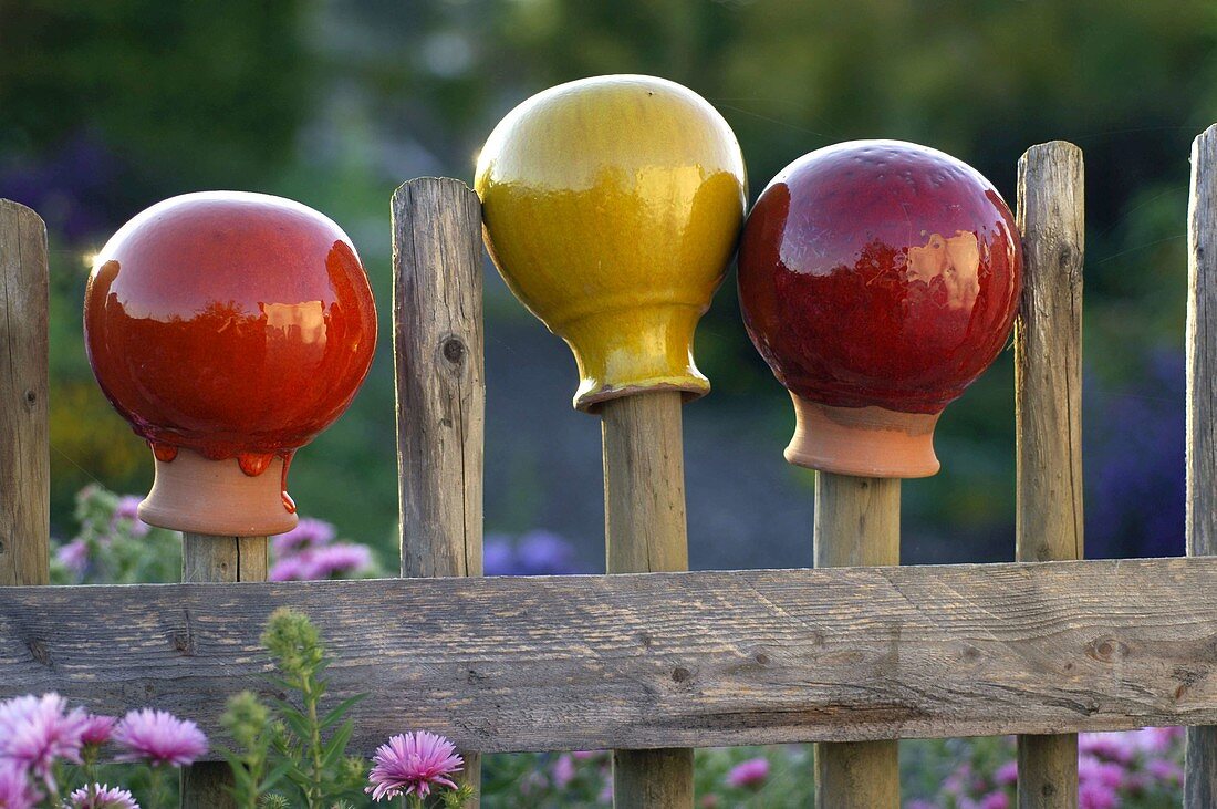 Garden balls of glazed terracotta on wooden fence