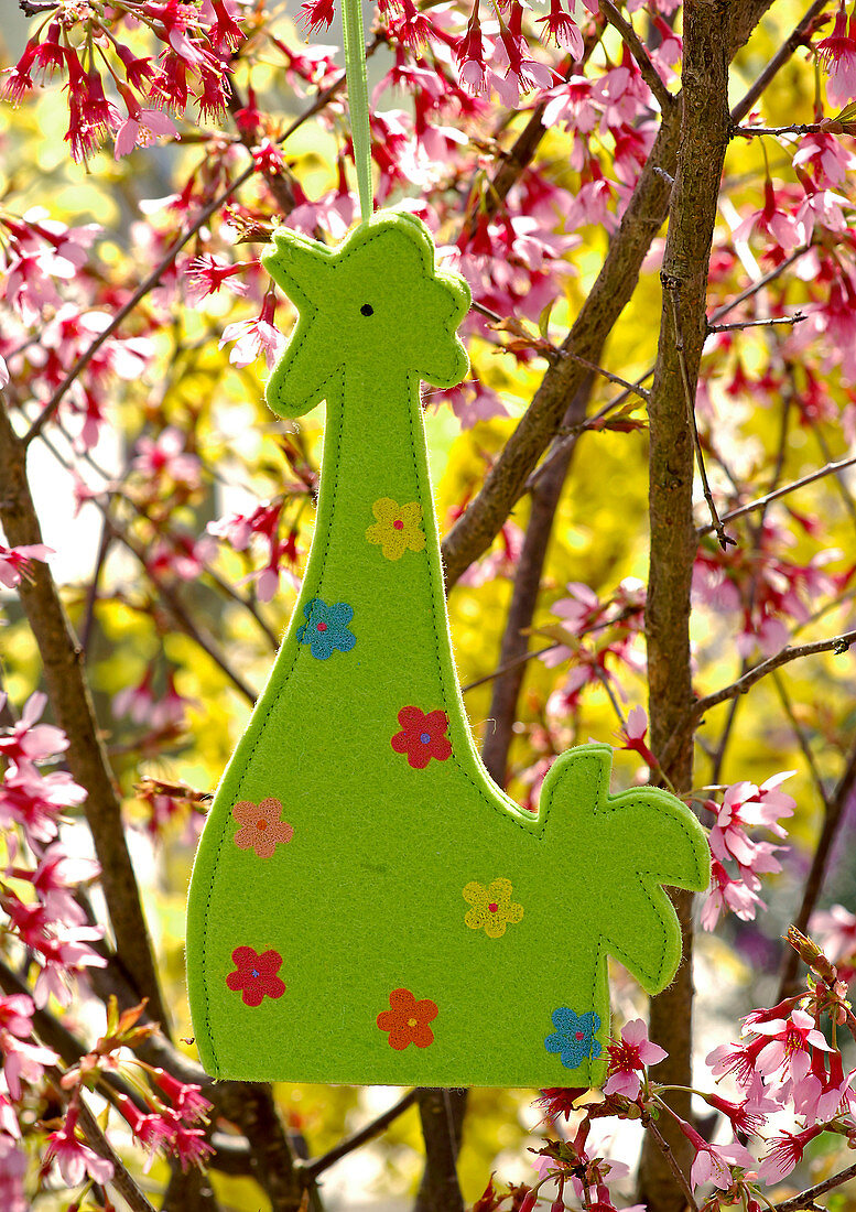 Hahn aus grünem Filz mit Blümchen an Prunus (Zierkirsche) aufgehängt