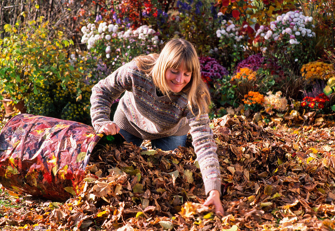 Young woman putting leaves into garden waste bag
