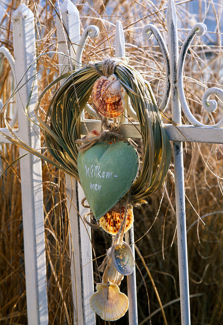 Wreath of grass with heart with message 'Welcome' on fence, shells