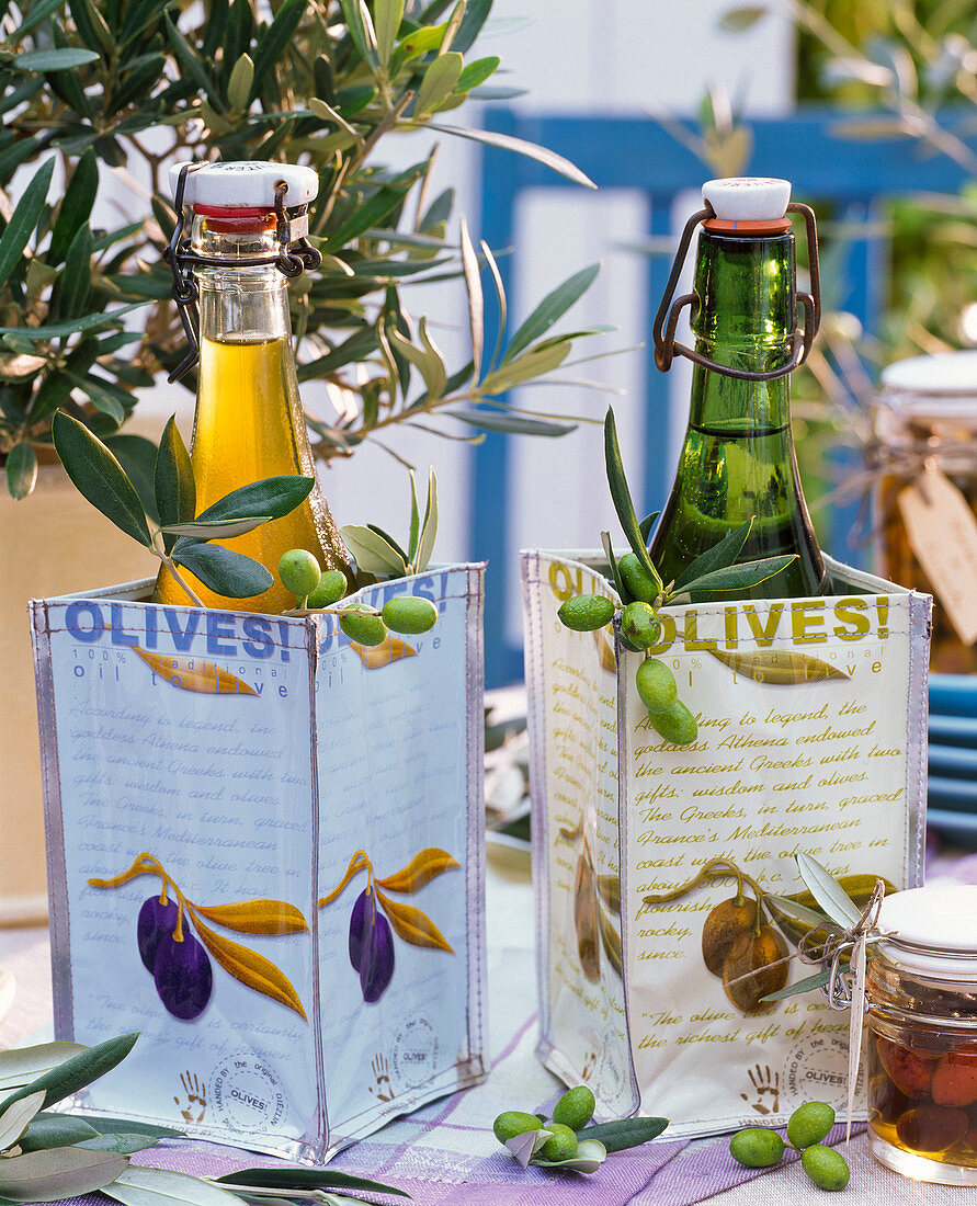 Bottles of olive oil in bags with olive motifs, branches and fruits of olea