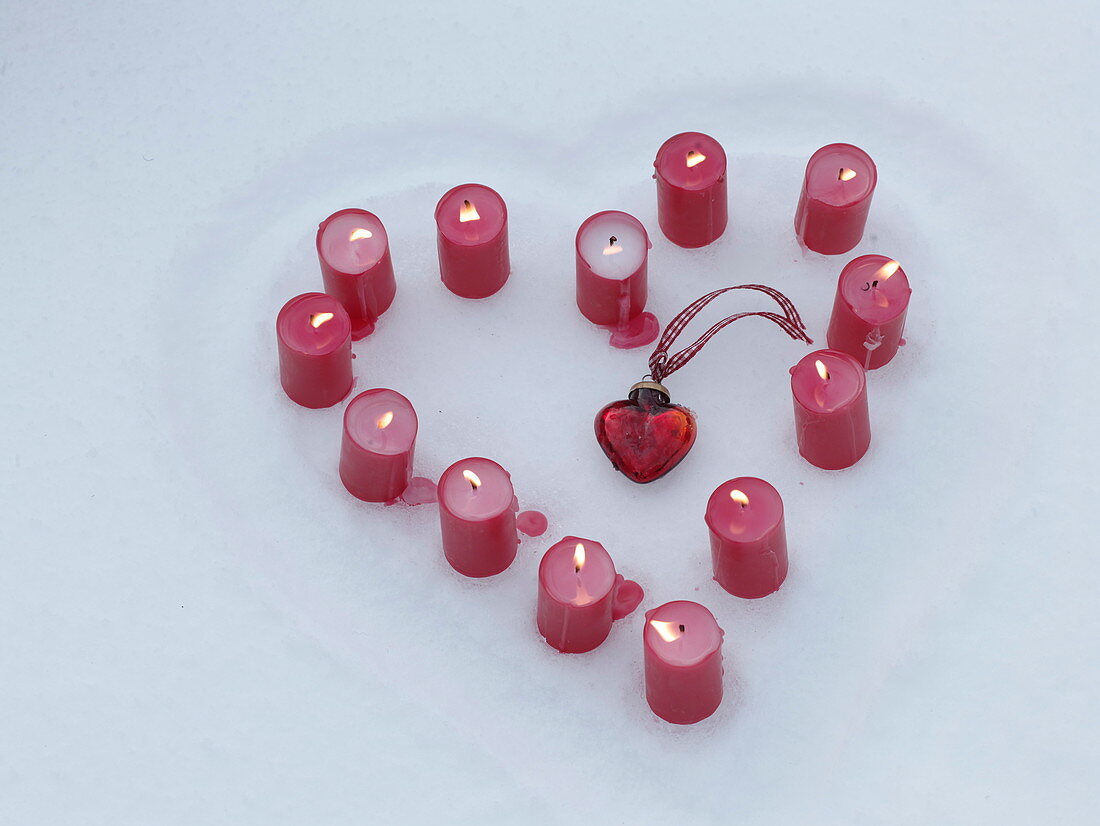 Heart of burning candles placed in a heart of snow, glass heart added