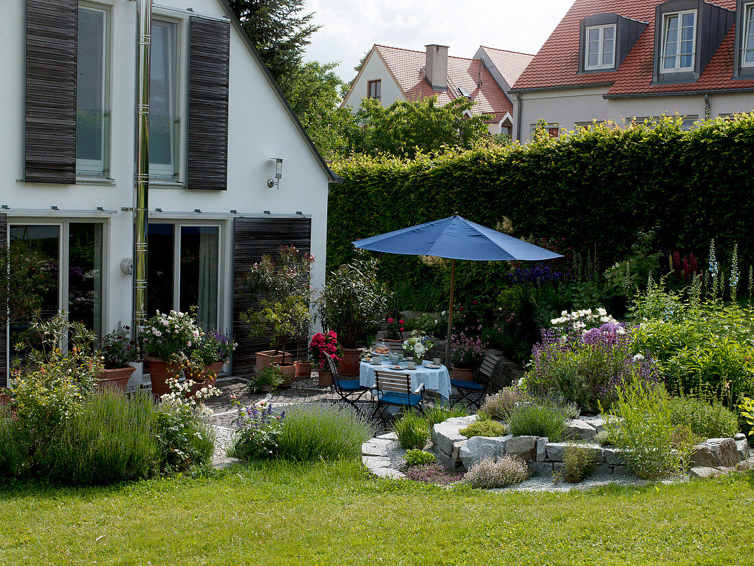 Blick vom Garten auf die Terrasse am Haus und die Kräuterspirale