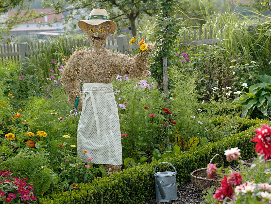 Scarecrow made of straw with straw hat and apron in the cottage garden