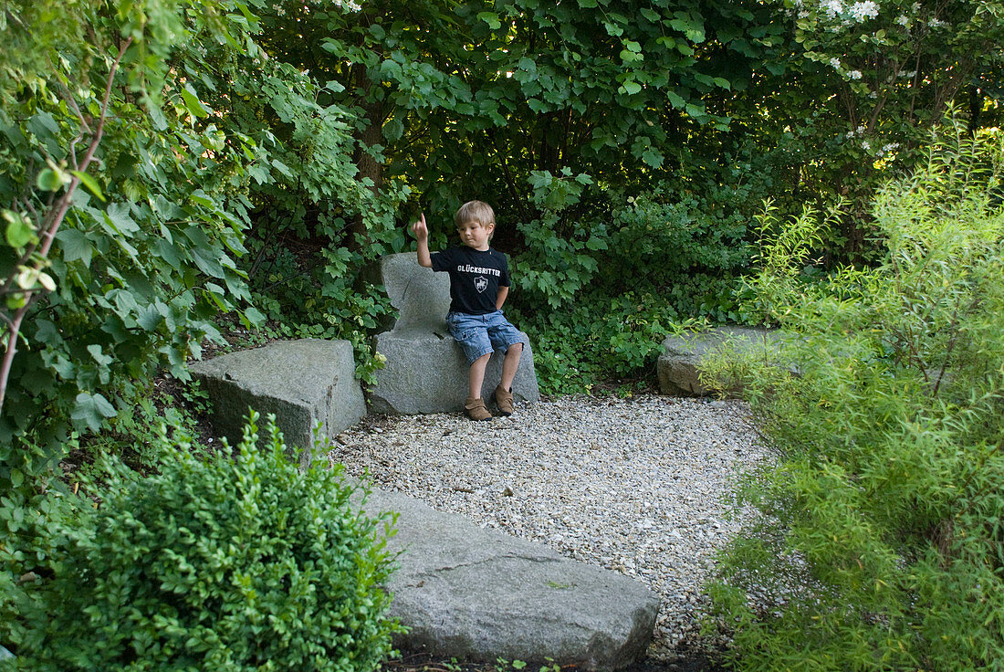 Small gravel square with granite blocks, boy sitting on stone chair