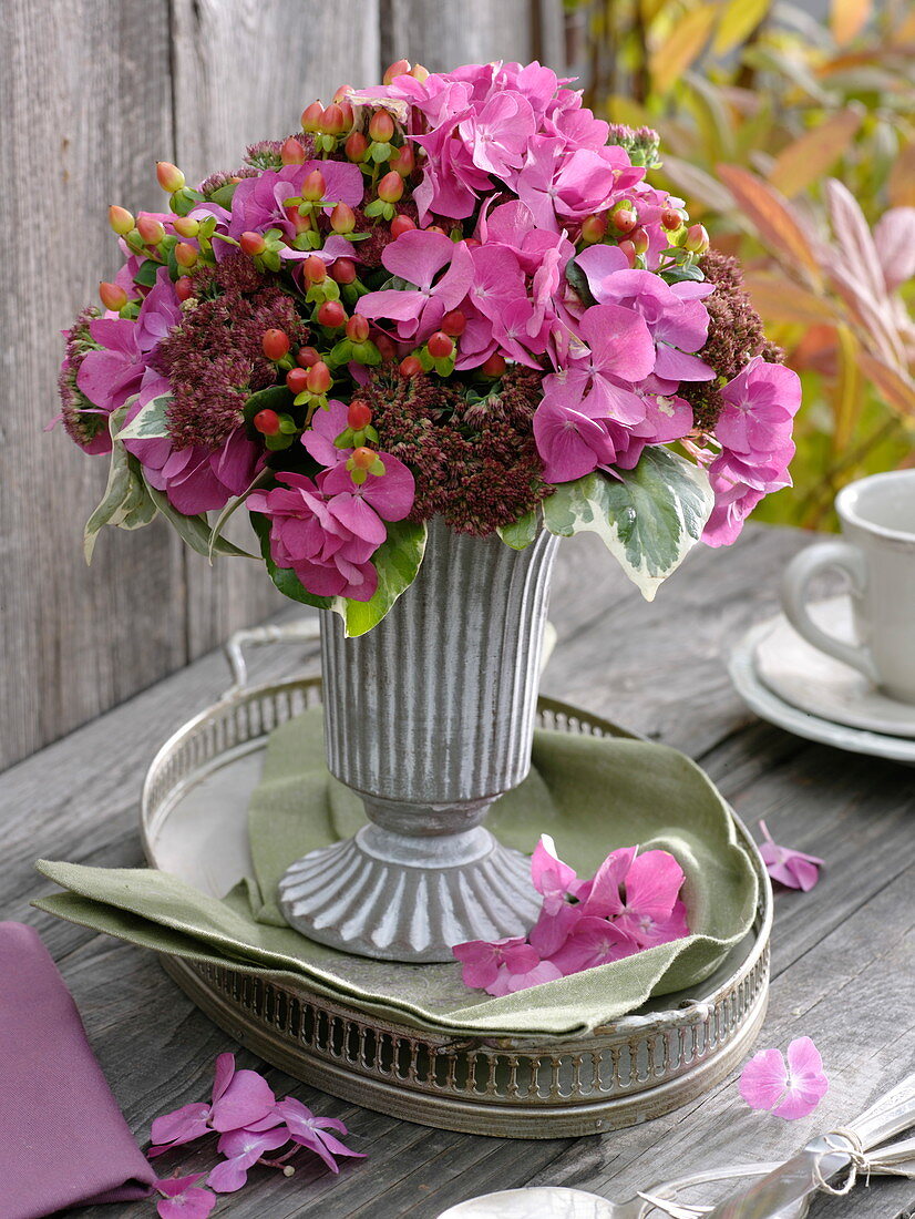 Bouquet with hydrangea, St. John's wort and stonecrop in metal vase with foot