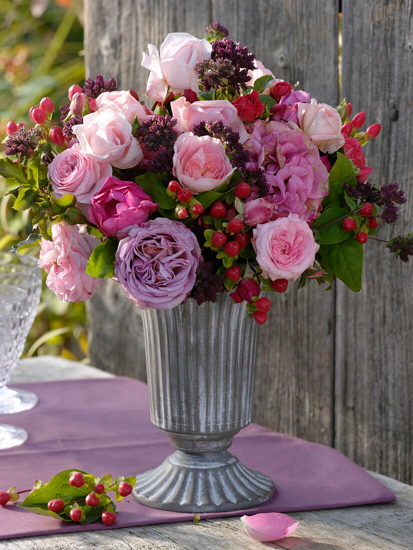 Rosenstrauß mit Johanniskraut und Oregano in Metallvase mit Fuß