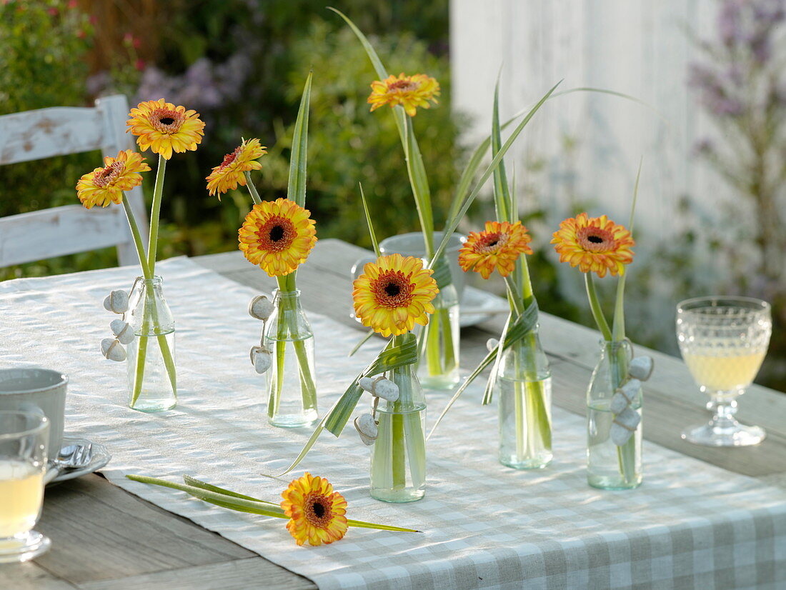 Modern table decorations with gerberas and grasses in small glass bottles