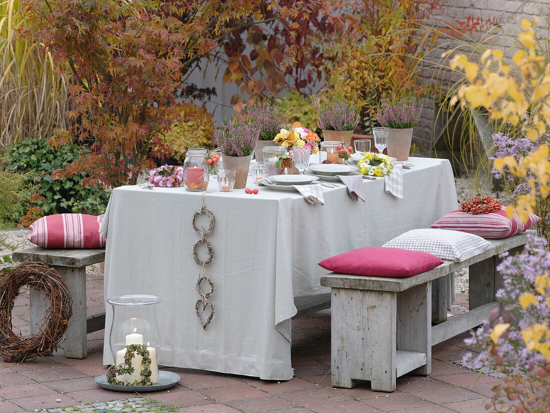 Herbstlich gedeckter Tisch mit Heide, Rosenstrauß und Chrysanthemenkränzen