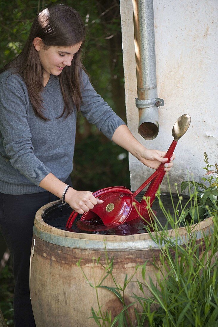 Frau schöpft Wasser aus Wasserfass