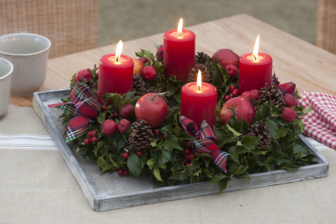 Advent wreath made of holly with red candles, apples and ornamental apples