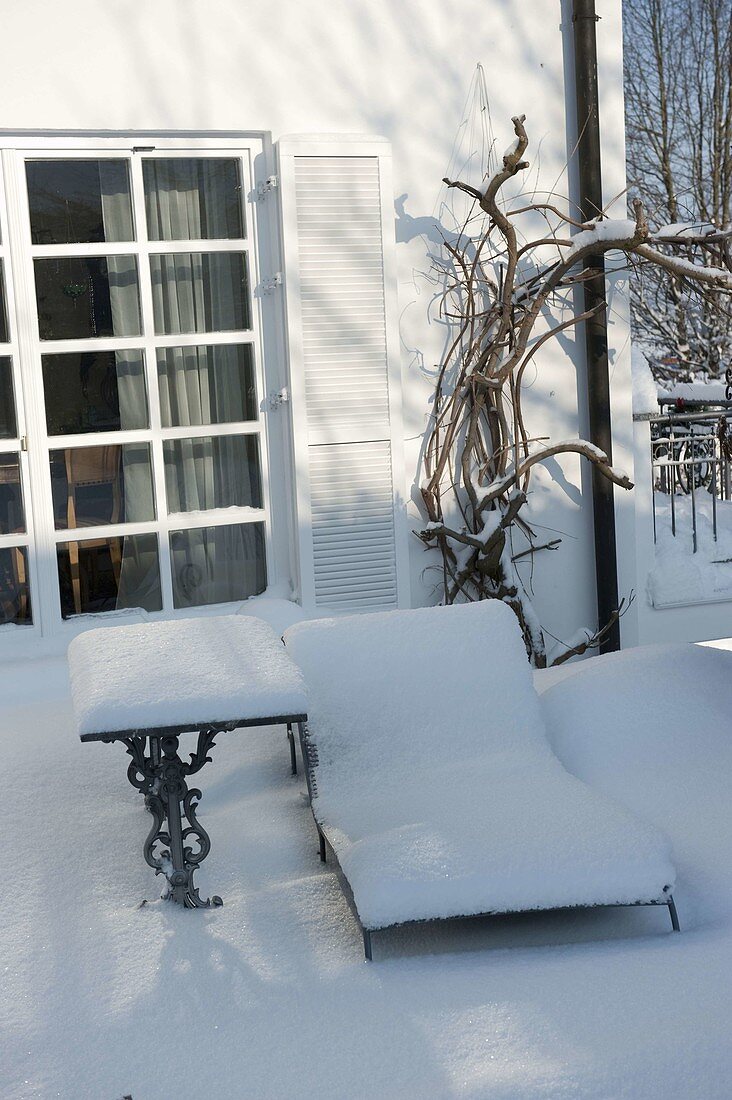 Verschneite Liege und kleiner Tisch auf Terrasse im Winter