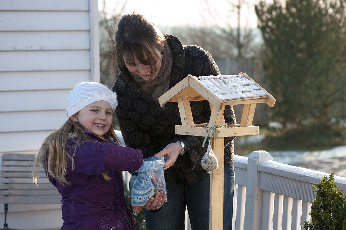 Mutter und Tochter befüllen ein Vogelfutterhaus