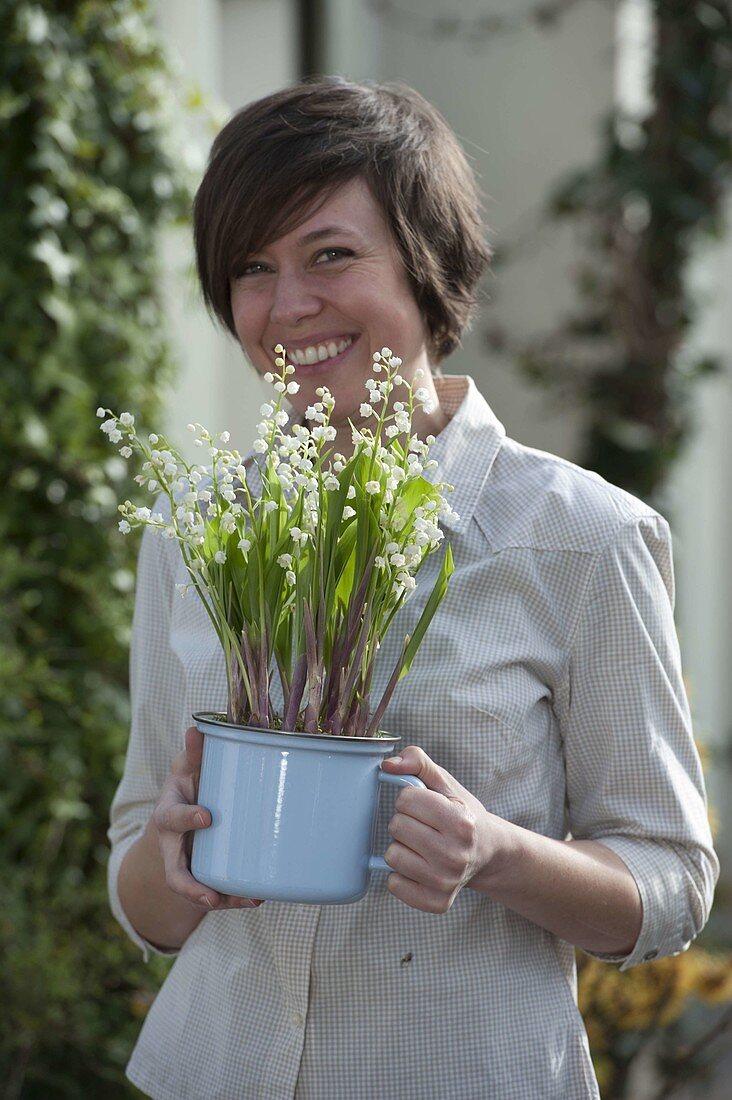 Frau mit emailliertem Topf mit Convallaria majalis (Maiglöckchen)