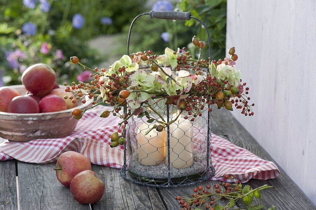 Glas-Windlicht im Drahtkorb mit Kranz aus Hydrangea (Hortensie) und Rosa