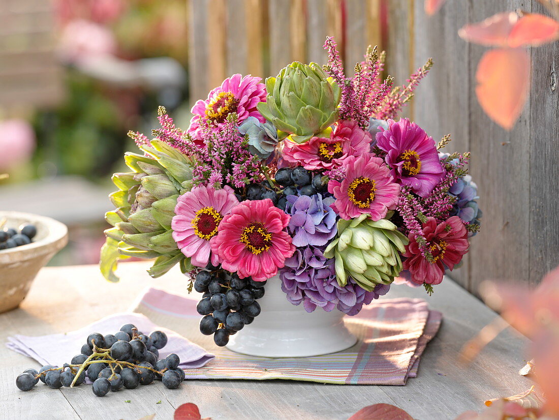 Herbstliches Gesteck in weißer Schale mit Artischocken (cynara), Zinnia