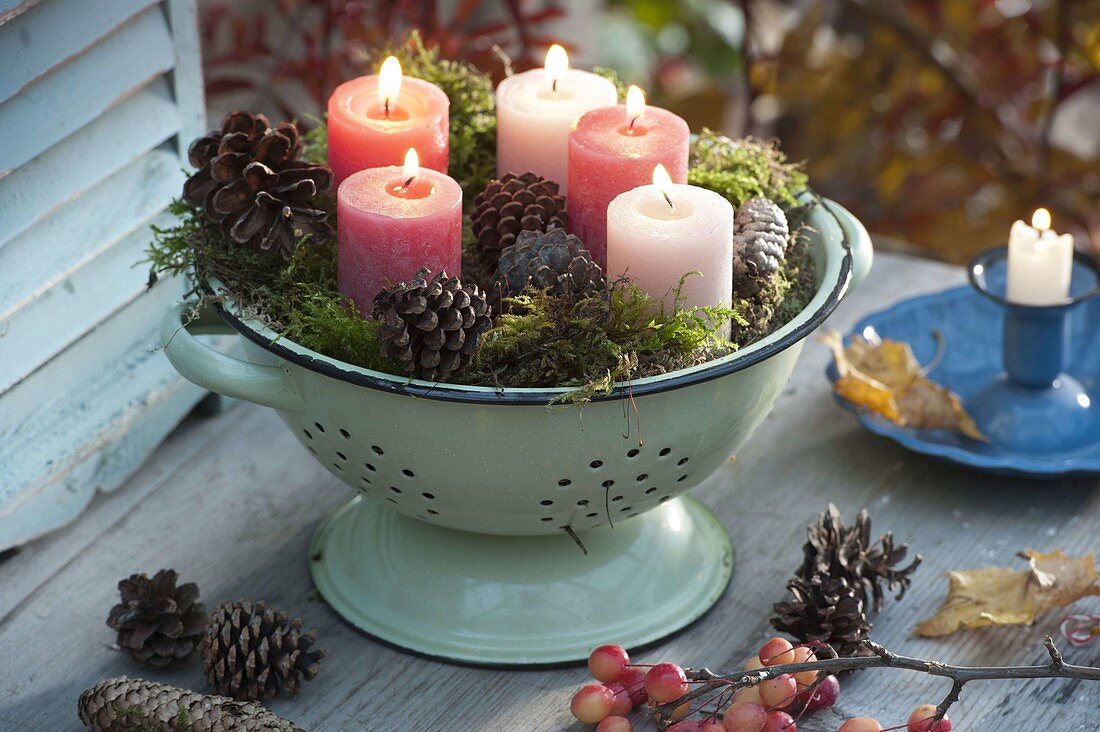 Candles in kitchen colander with moss and cones