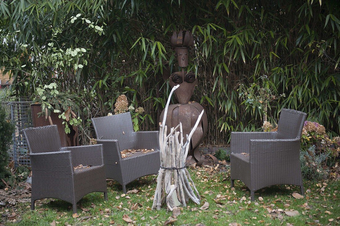 Lantern made of driftwood, female figure made of Corten steel in front of bamboo hedge