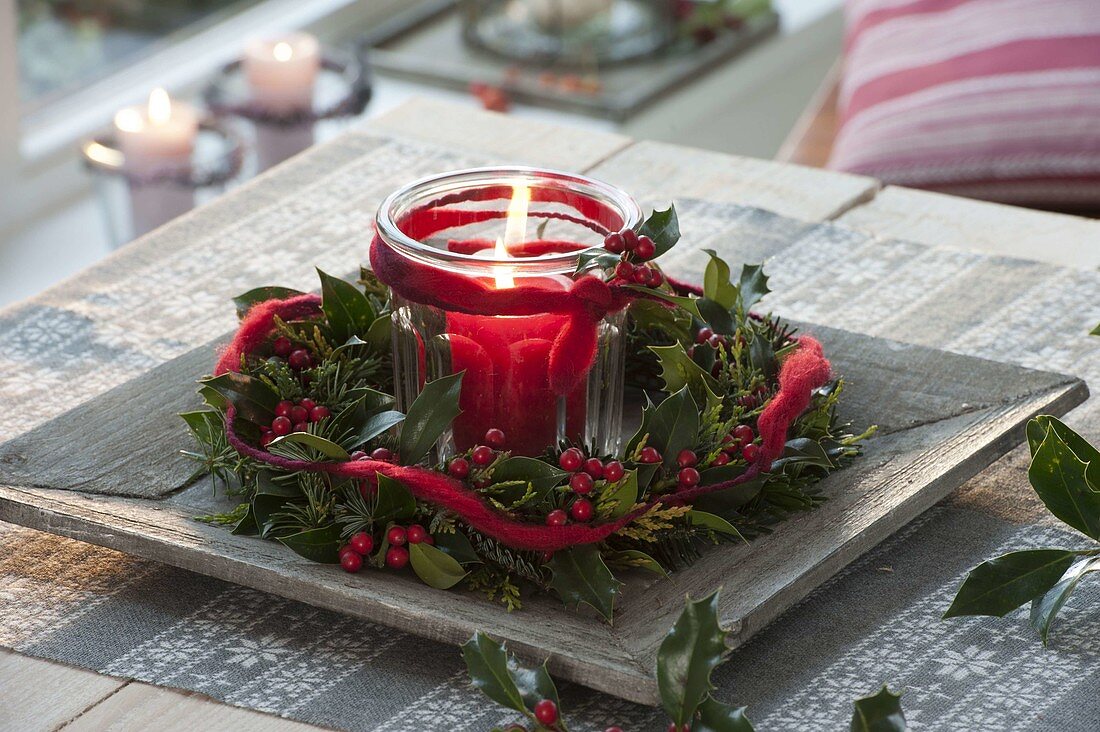 Glass with red candle as a lantern in a wreath of Ilex (holly), Abies