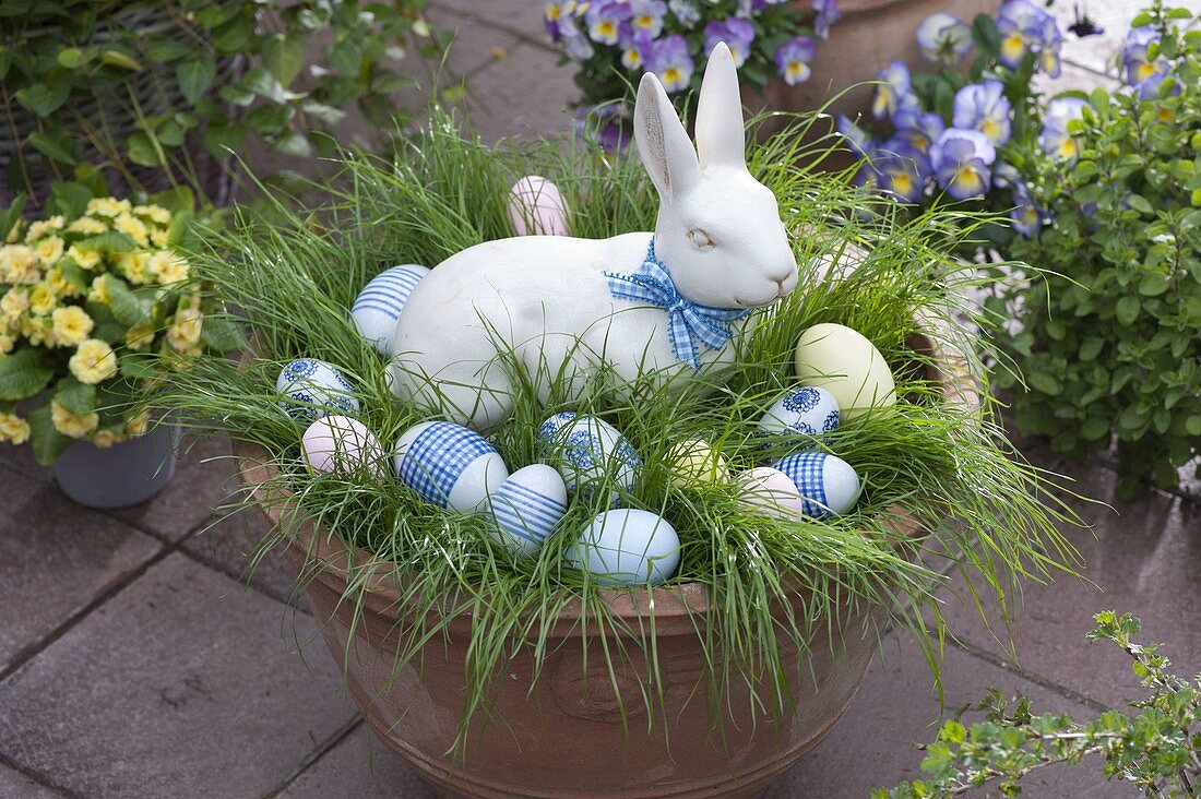 Pot with grass as Easter nest with ceramic Easter bunny and Easter eggs in blue and white