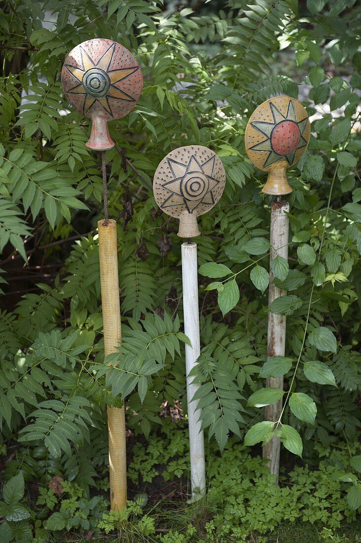 Pottery garden sticks 'Suns' on wooden sticks in a flower bed