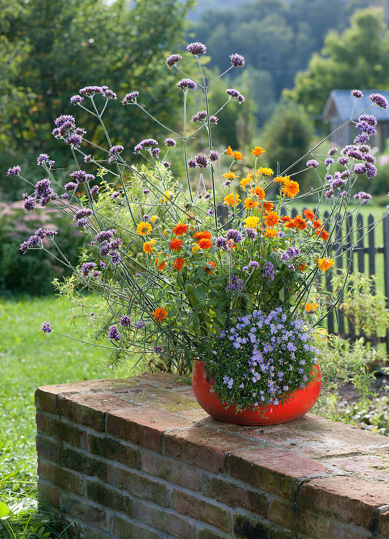 Woman plants red bowl with summer flowers