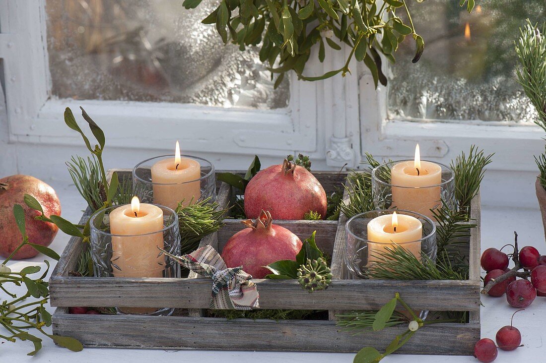 Wooden box with candles in glasses, pomegranates (Punica granatum)