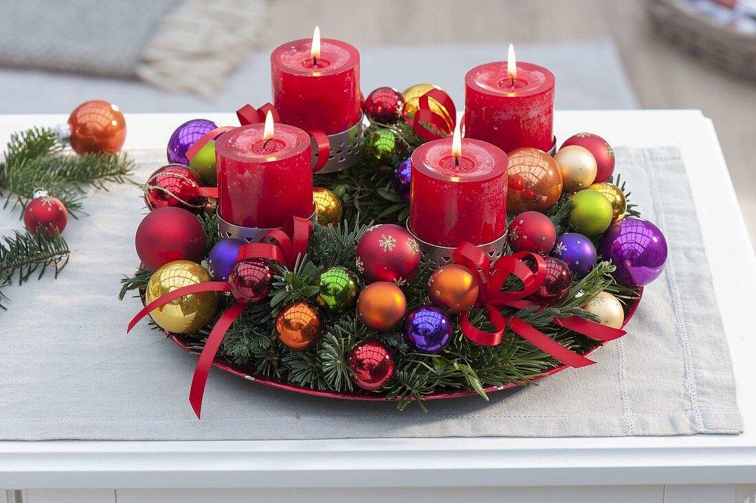 Bunter Adventskranz mit roten Kerzen in silbernen Haltern, bunte Kugeln