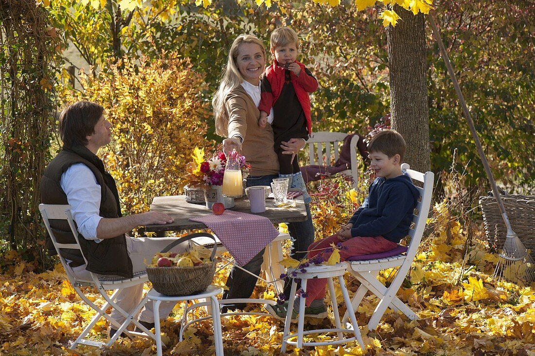 Family at table in golden autumn leaves under maple tree