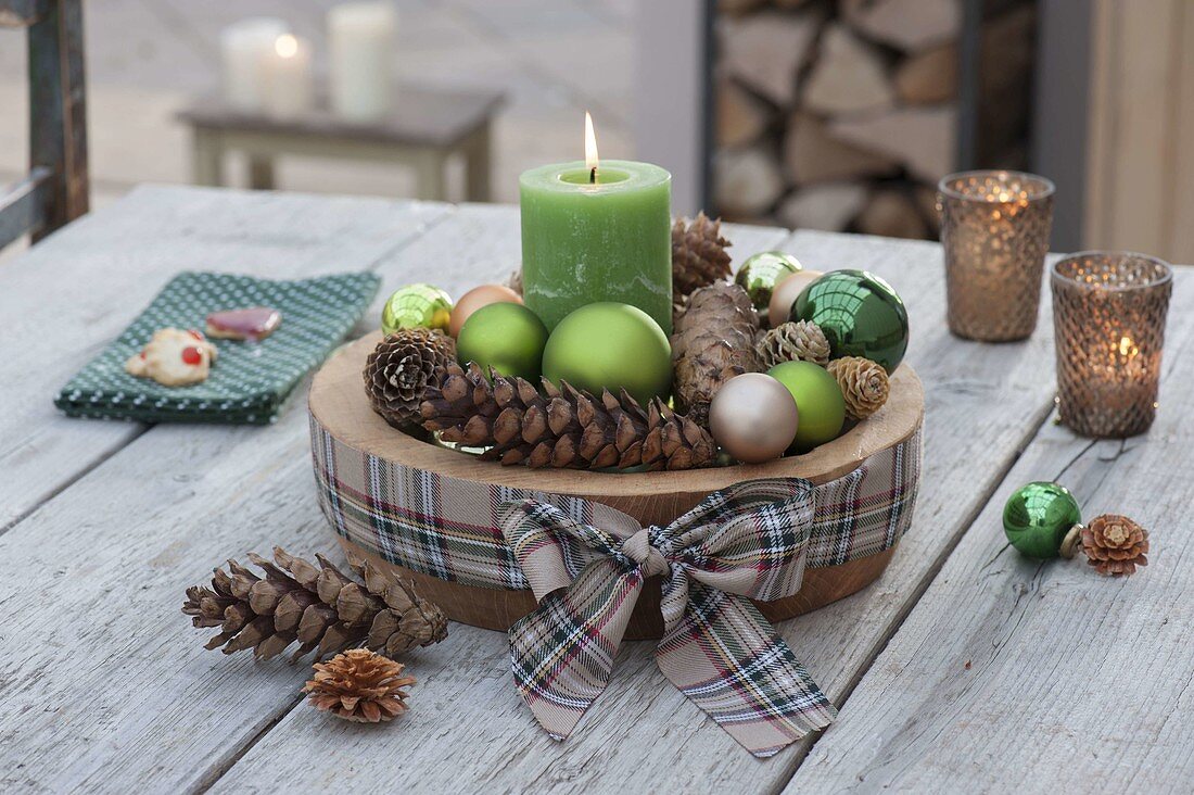Advent decoration with green candle, balls and cones in wooden bowl