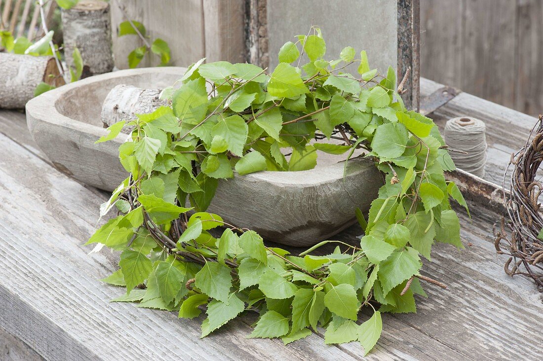 Maiengrün wreath with Betula branches leaning against wooden bowl