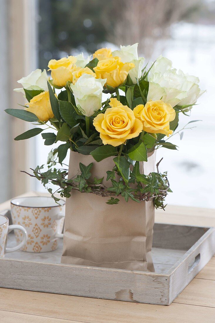 Yellow-white rose bouquet in paper bag with Hedera tendril