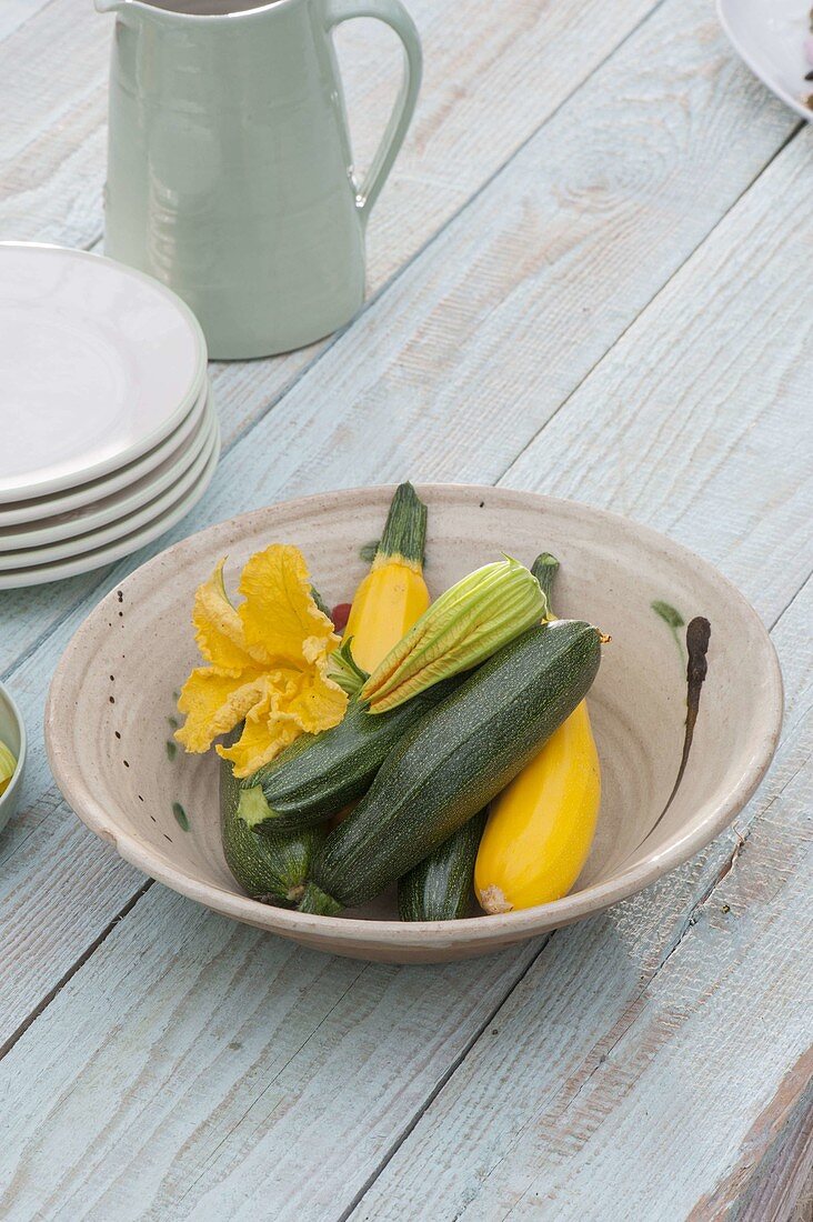 Freshly harvested green and yellow courgettes and flowers in bowl