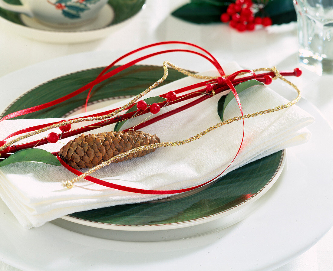 Napkin decoration: red sticks with threaded holly berries and leaves