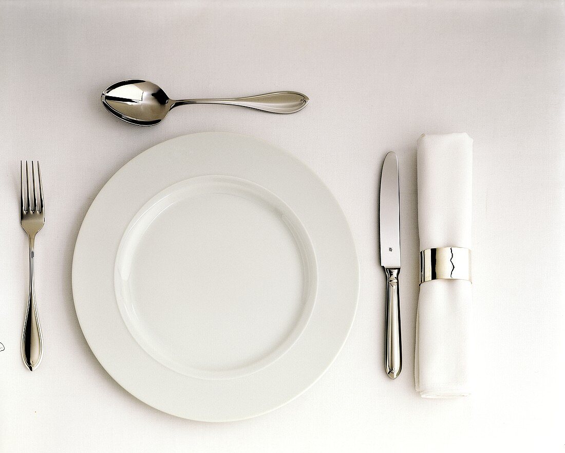 Ein Gedeck mit weißem Teller, Besteck & Serviette