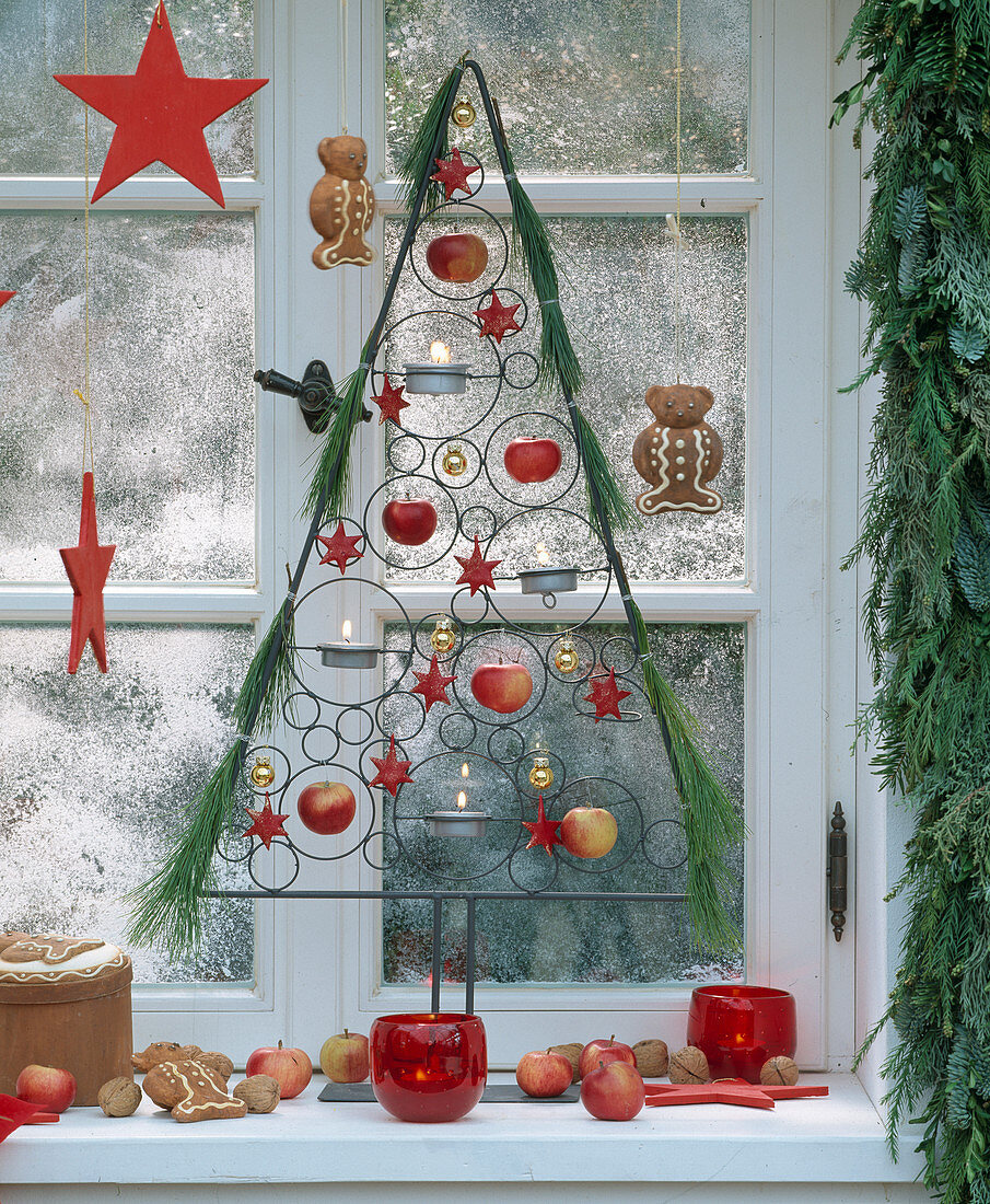 Weihnachtlich geschmücktes Fenster mit Äpfeln, Sternen und Girlande aus Zweigen