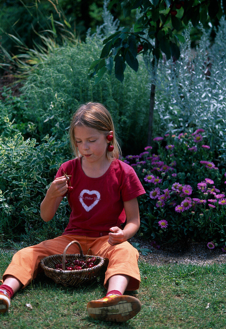 Girl sitting in the meadow and eating cherries