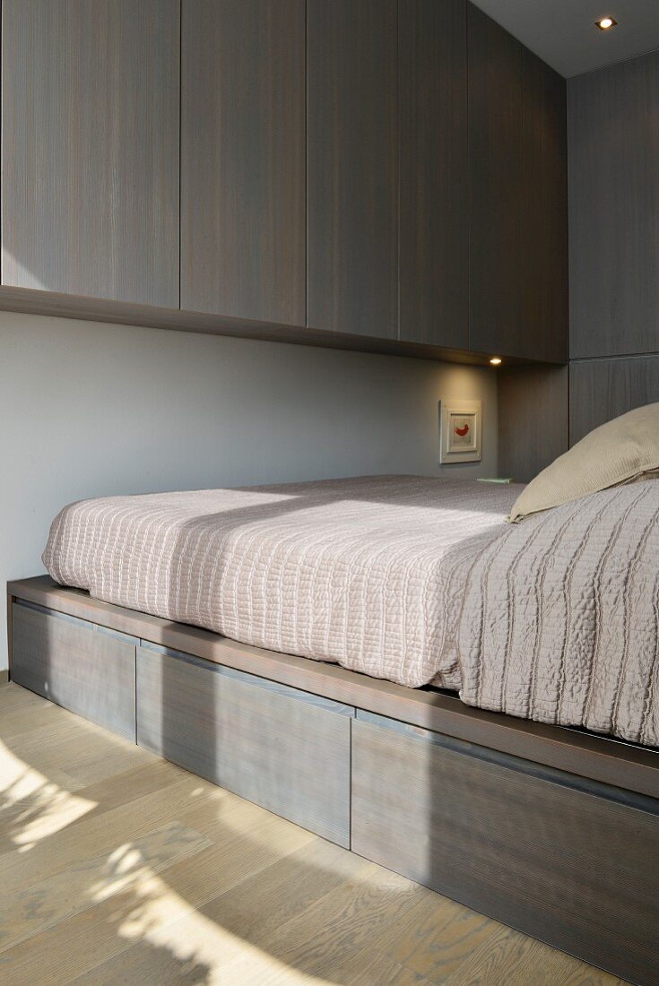 Fitted cupboards and bed on top of storage drawers in minimalist bedroom