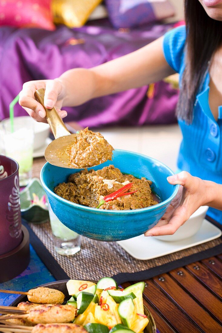 Asiatische Frau serviert Beef Radang (Rindfleischgericht, Indonesien)