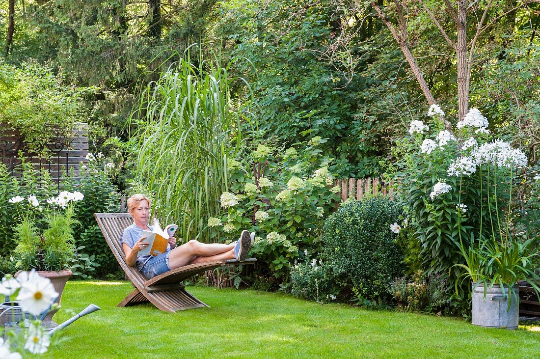 Woman reading on wooden lounger in well-tended garden