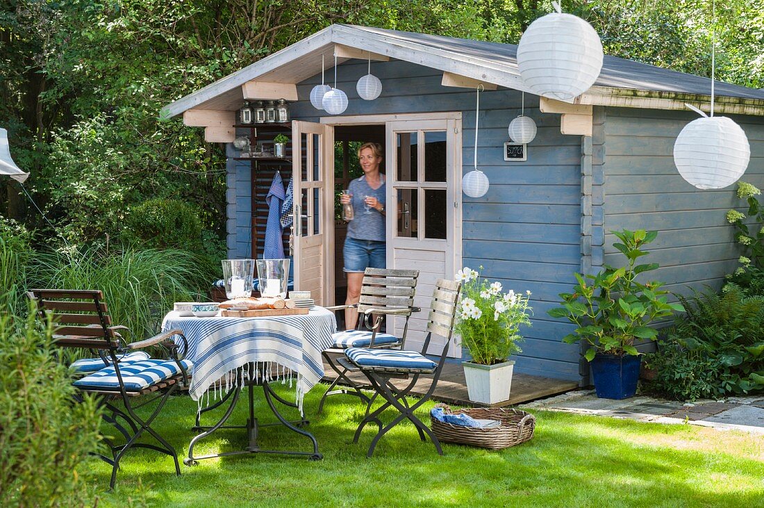 Idyllic seating area with many lanterns in front of summer house with woman in open door